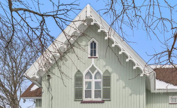 A light green house gable with white decorative vergeboard trim, a central pointed-arch window, and bare winter trees.