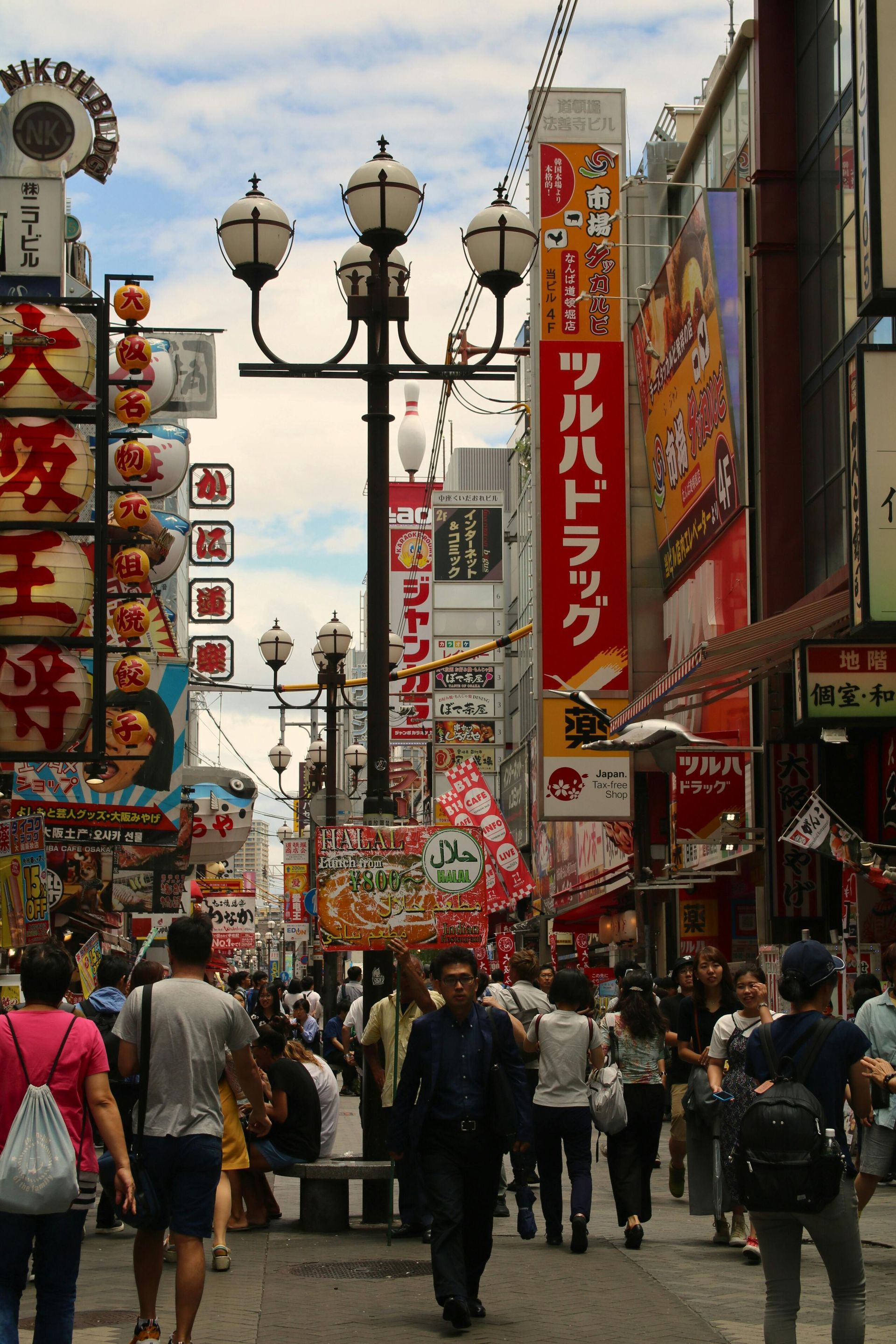 Mensen lopen door een drukke, smalle straat in Osaka, Japan, met hoge gebouwen, felle reclameborden en straatlantaarns.