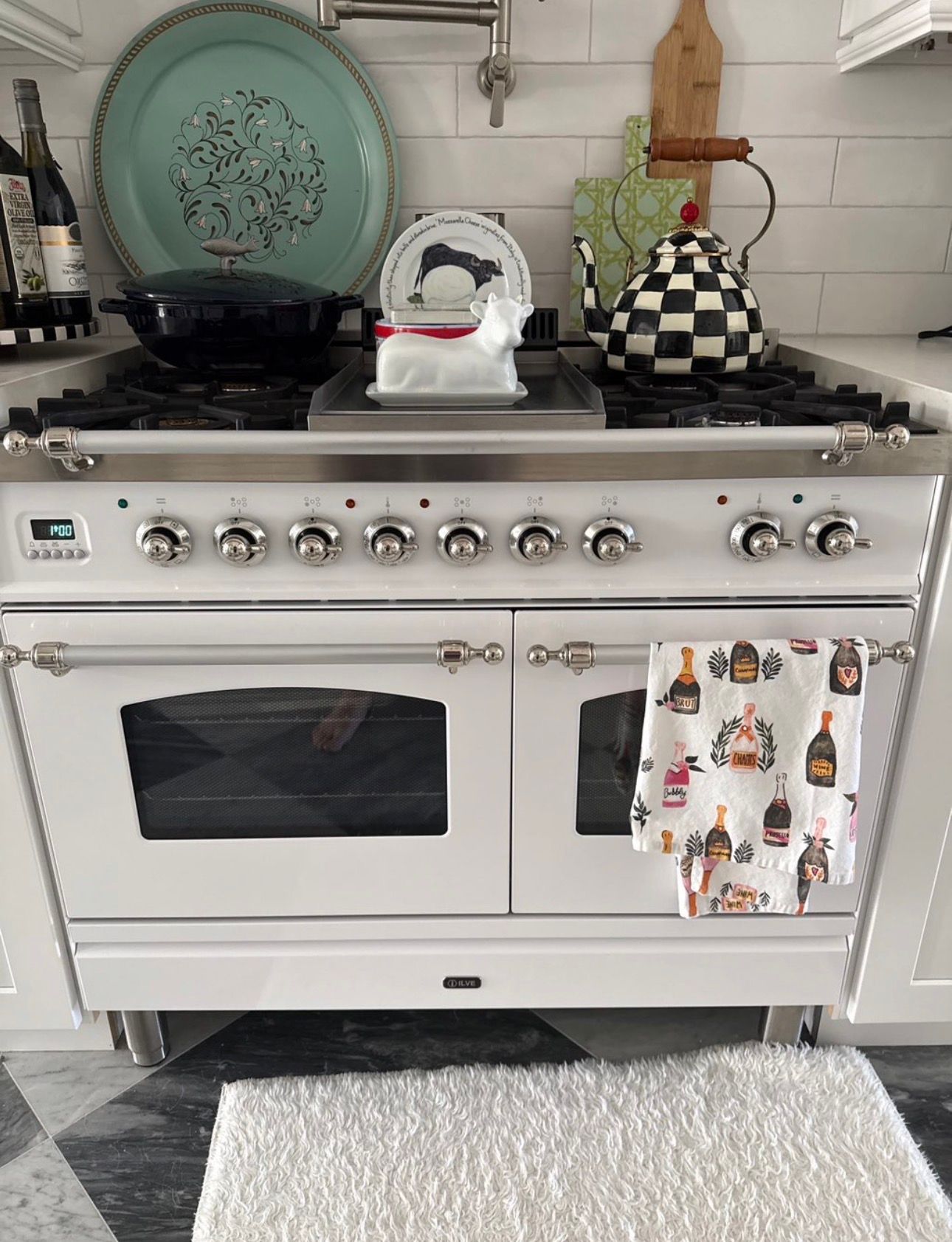 White kitchen stove with silver knobs, checked teapot, green plate, and patterned towel hanging on the oven handle