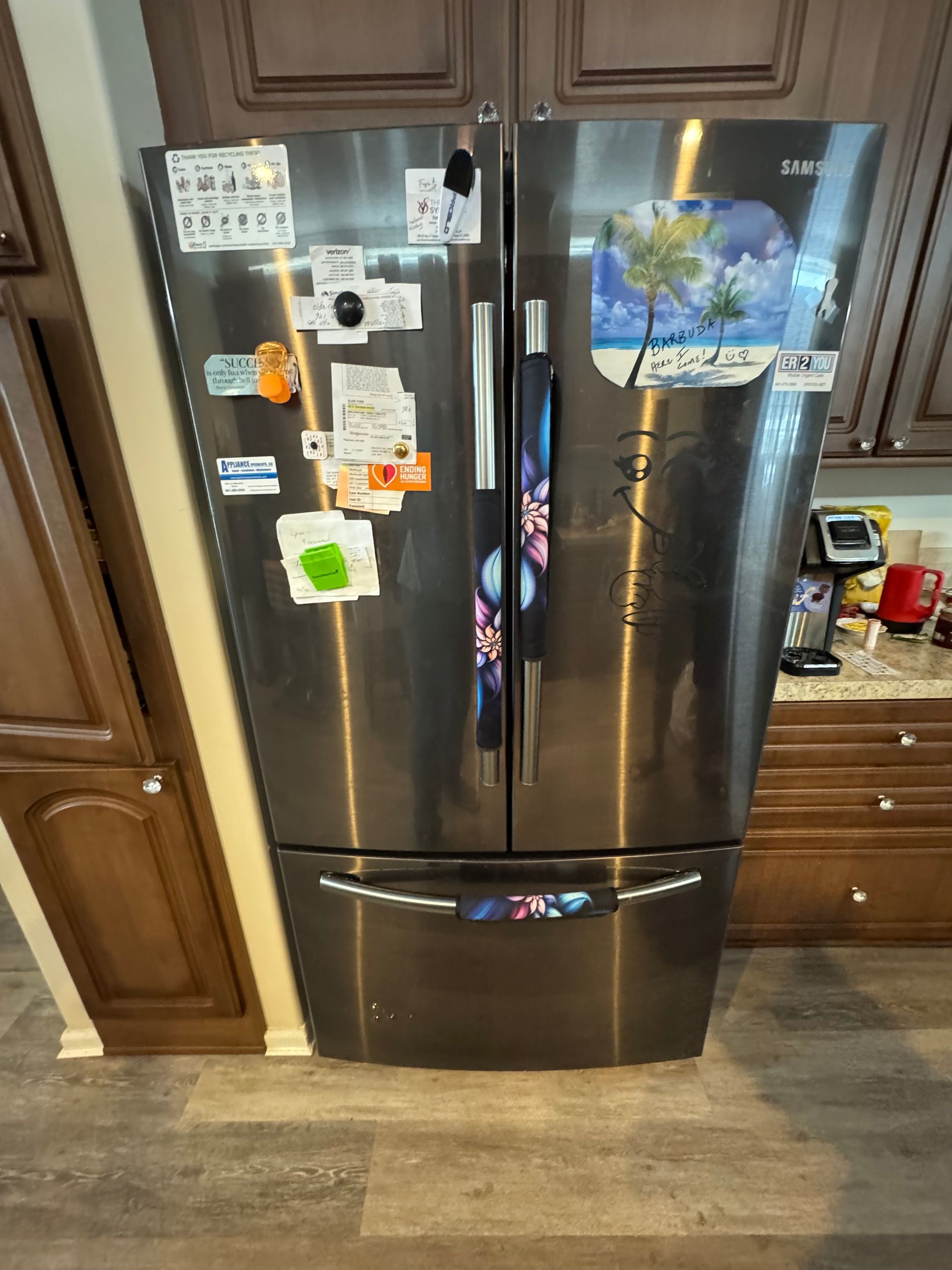 Stainless steel French-door refrigerator with magnets and photos in a kitchen.