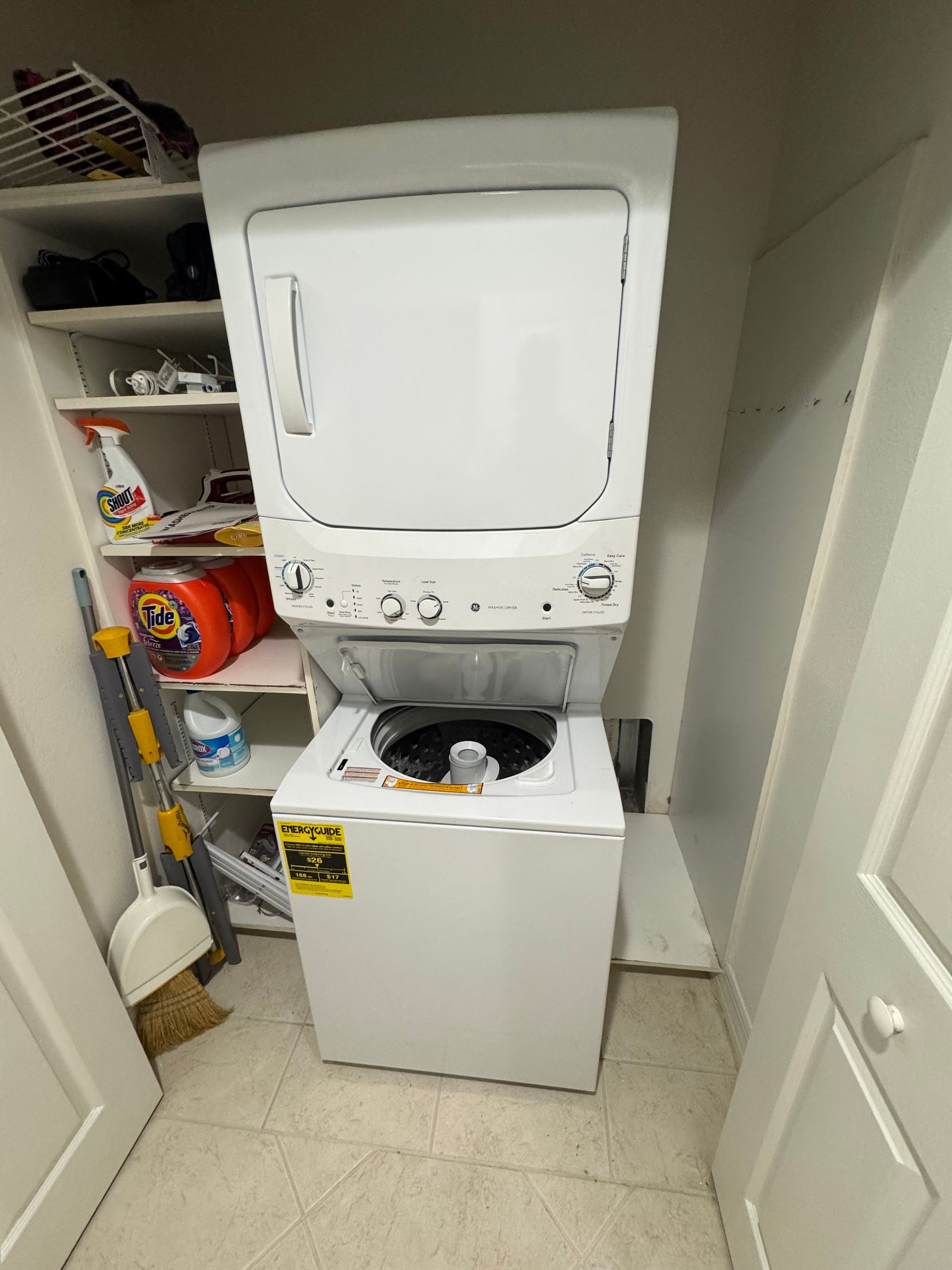 Stacked washer and dryer in a laundry closet with open storage shelves beside it.