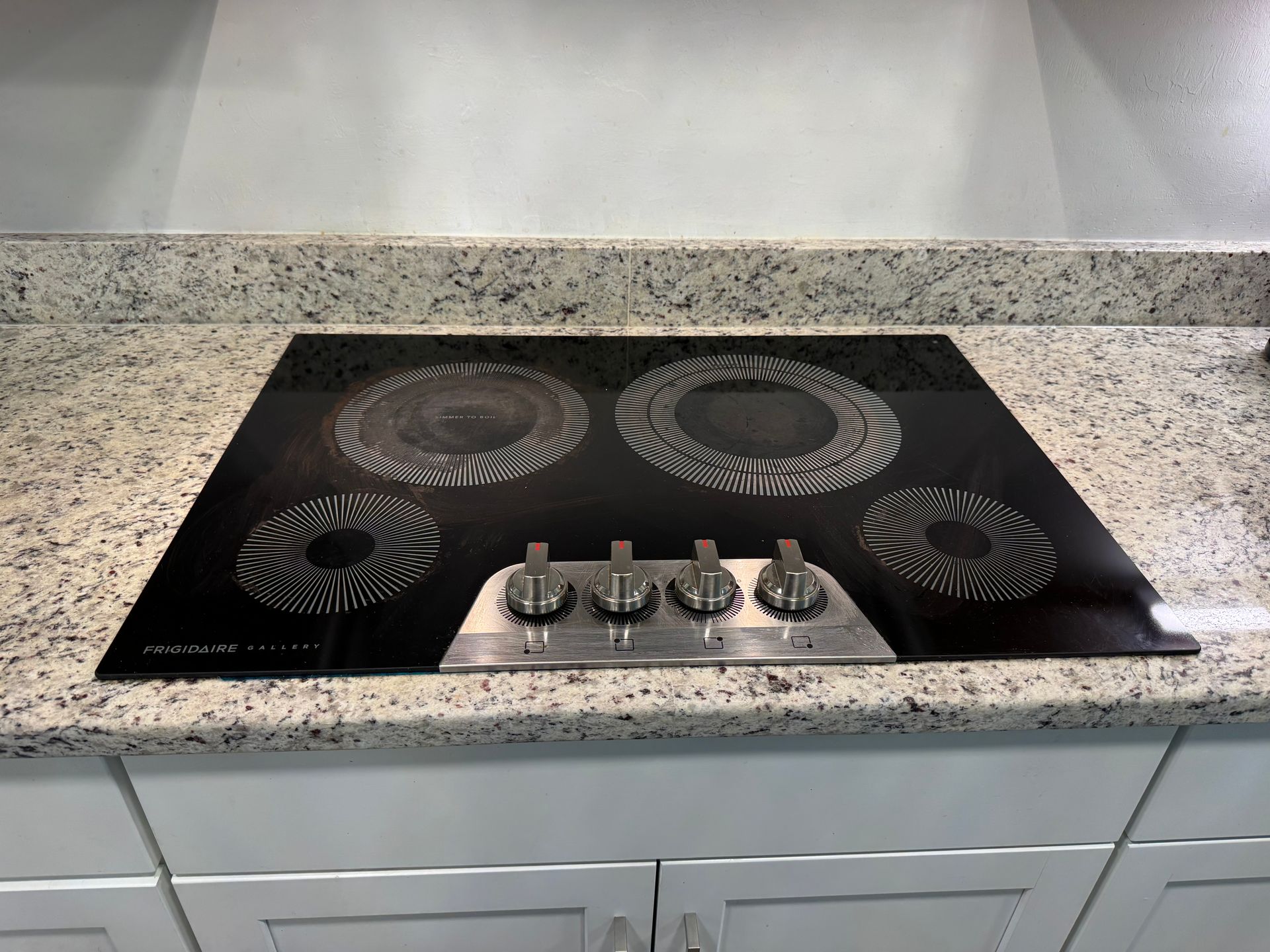 Black glass electric cooktop with four burners and front control knobs on a kitchen counter