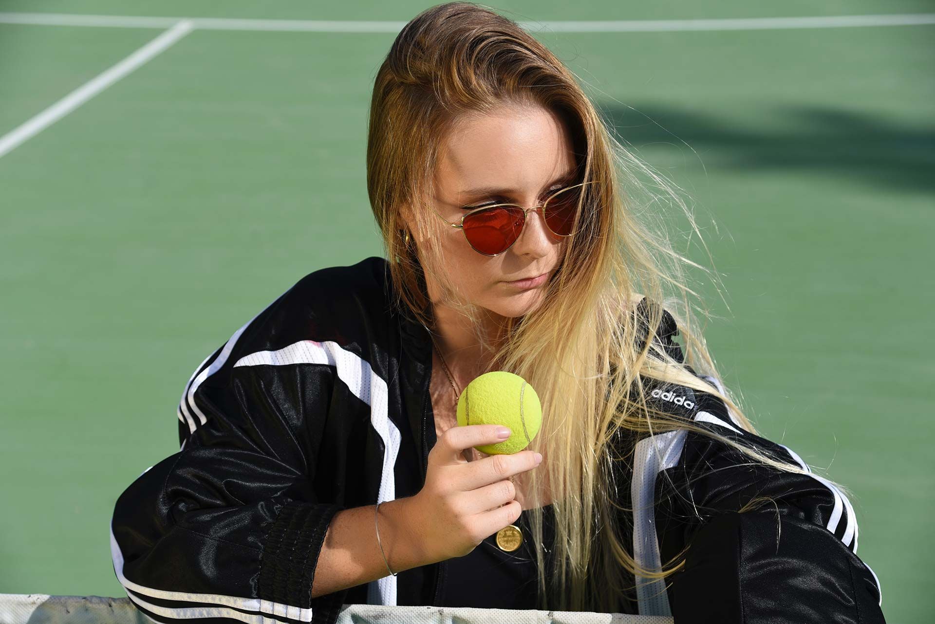 Une femme portant des lunettes de soleil tient une balle de tennis sur un court de tennis.