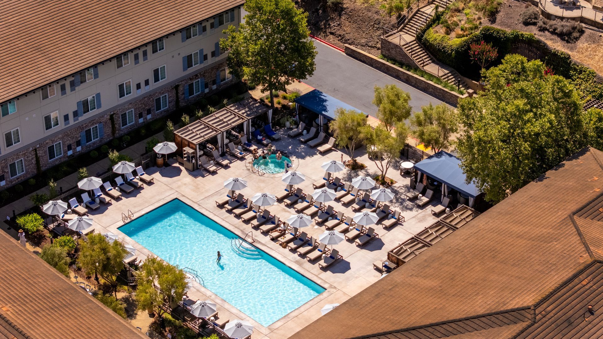 Aerial view of a hotel courtyard with a swimming pool, lounge chairs, and umbrellas surrounded by buildings.