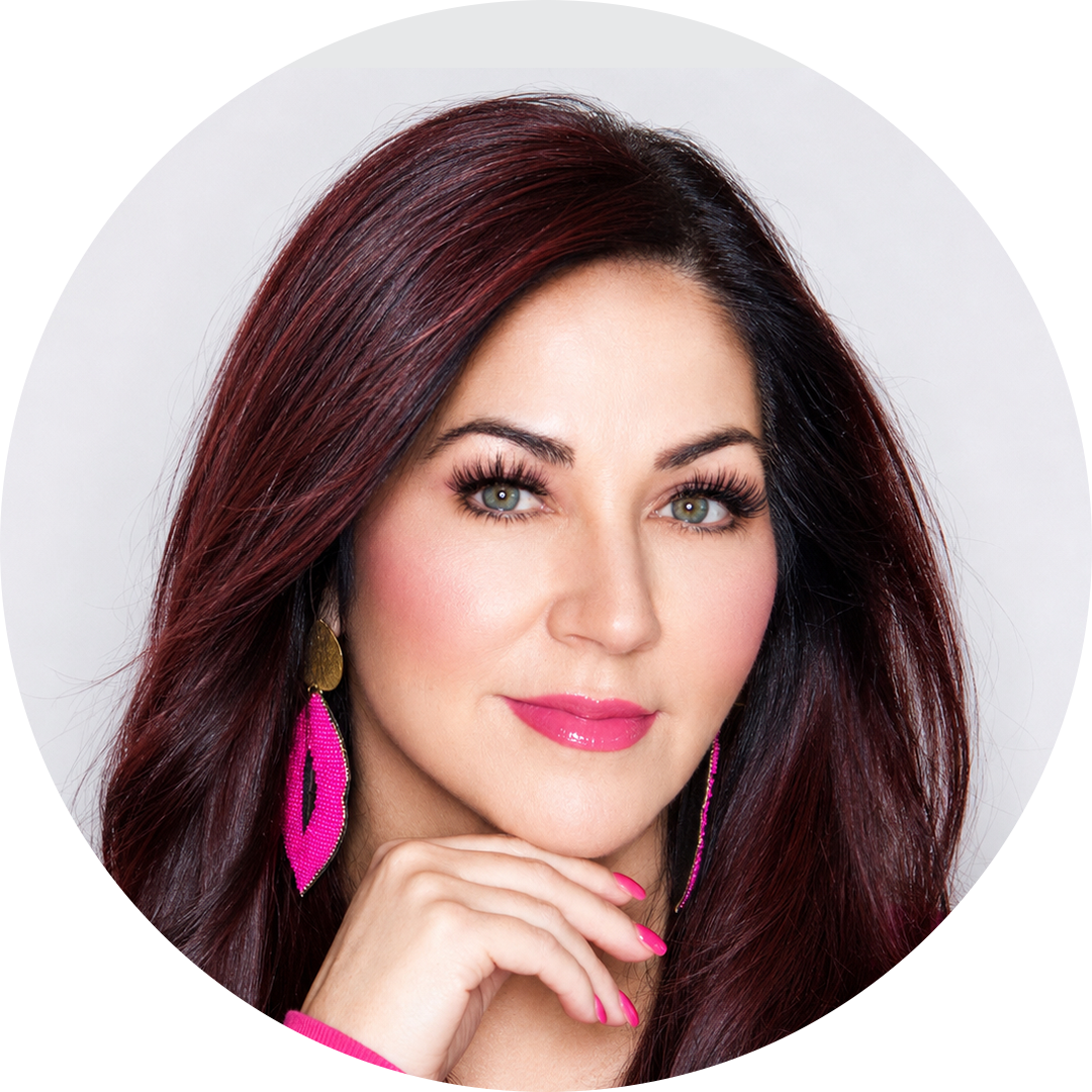 Studio headshot of a woman with dark hair, pink earrings, and a pink top, resting her chin on her hand.