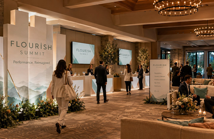 Conference networking event in a hotel ballroom with a stage, banners, and attendees mingling