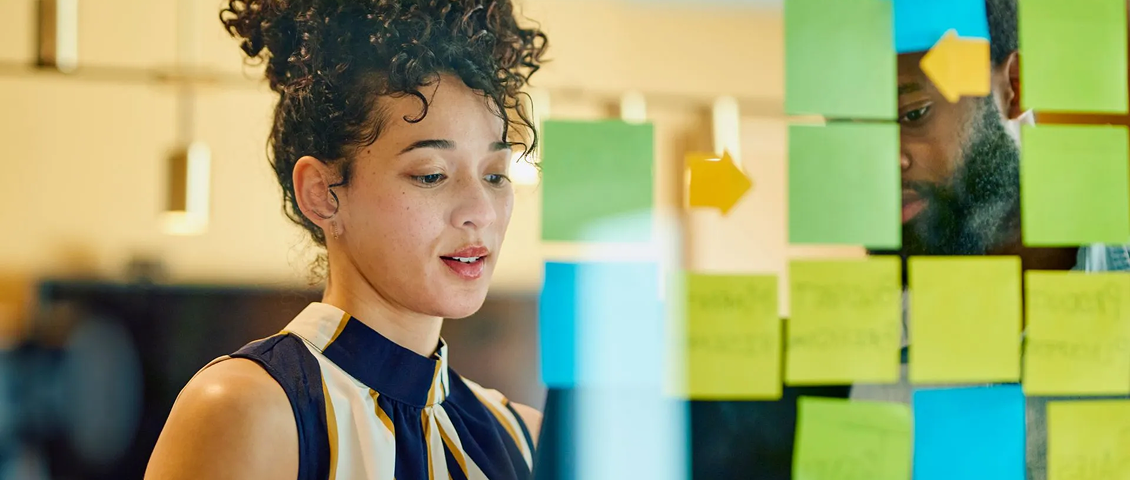 Person writing on colorful sticky notes on a glass wall in an office setting