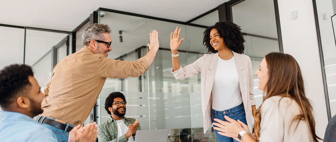 Colleagues high-five in a bright office during a team meeting