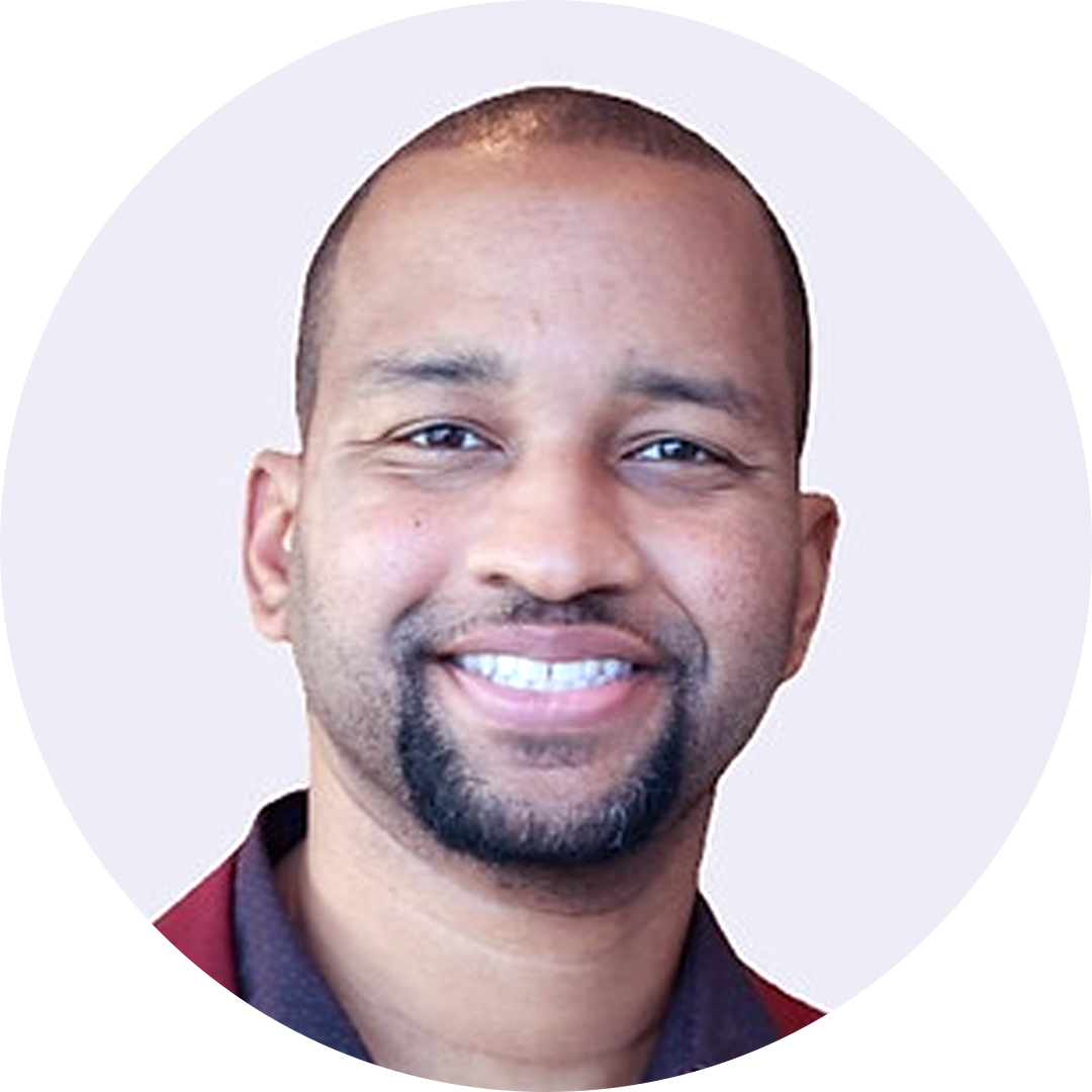 Smiling man with a shaved head and goatee against a light circular background