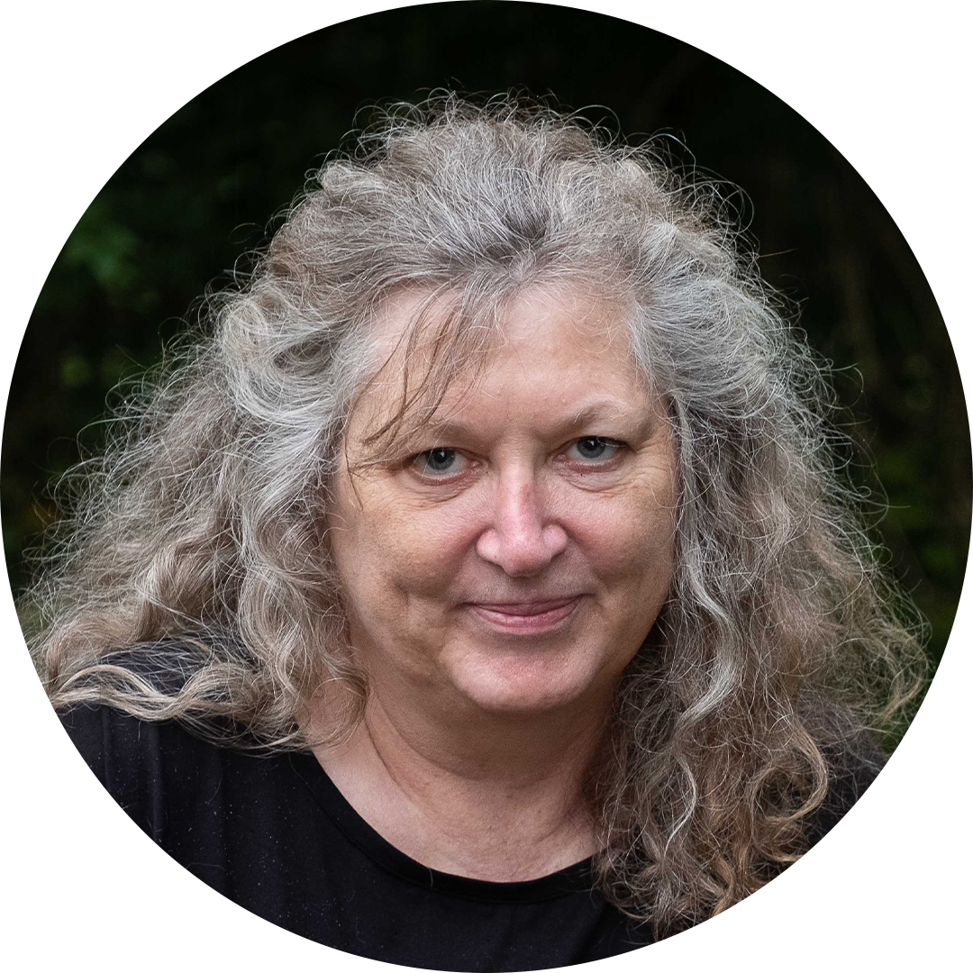 Portrait of a person with curly gray hair, wearing a black top, against a dark outdoor background