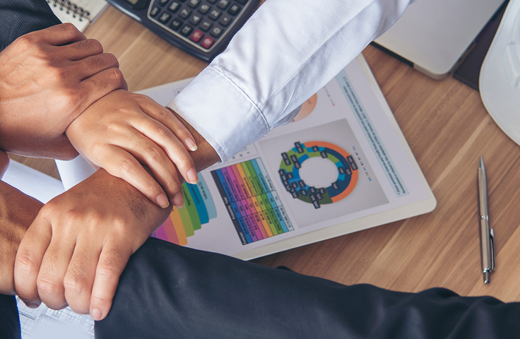 Hands stacked over a tablet showing colorful charts and a pie graph on a desk