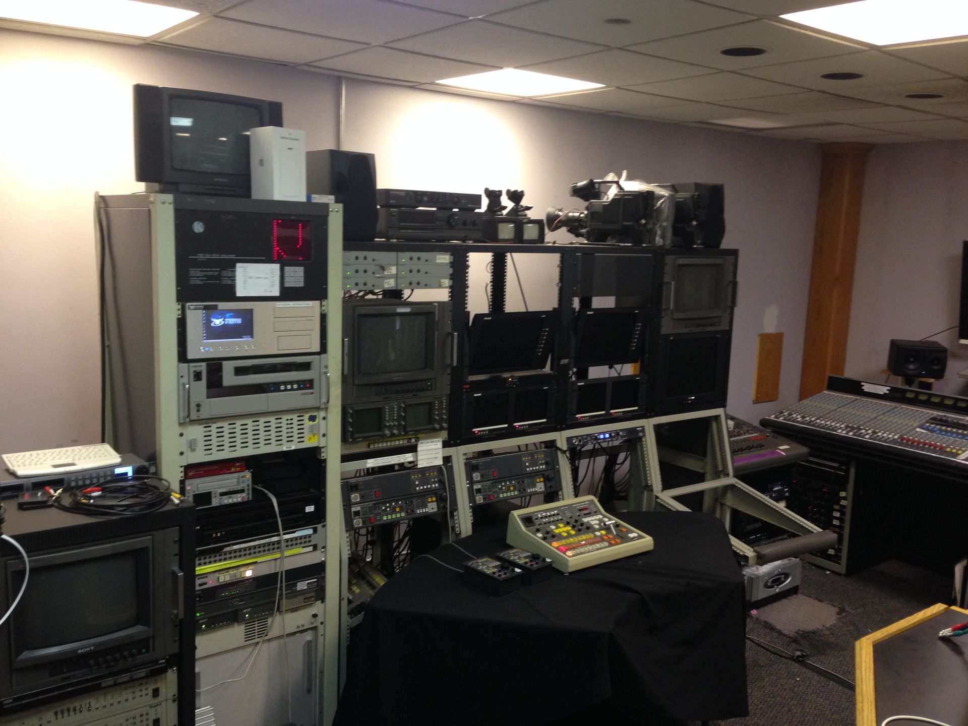 Television studio equipment, rack-mounted electronics, monitors, mixing console, broadcast equipment.