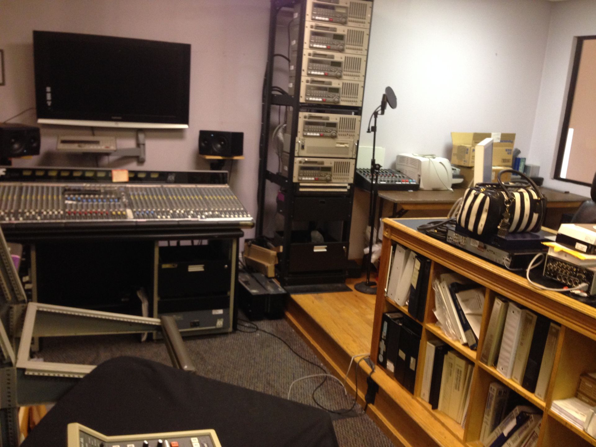 Recording studio with a mixing console, rack of equipment, shelves, and a microphone.