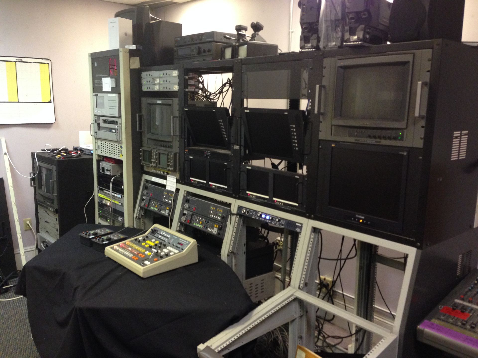 A control room with equipment racks, monitors, and a mixing console on a table.