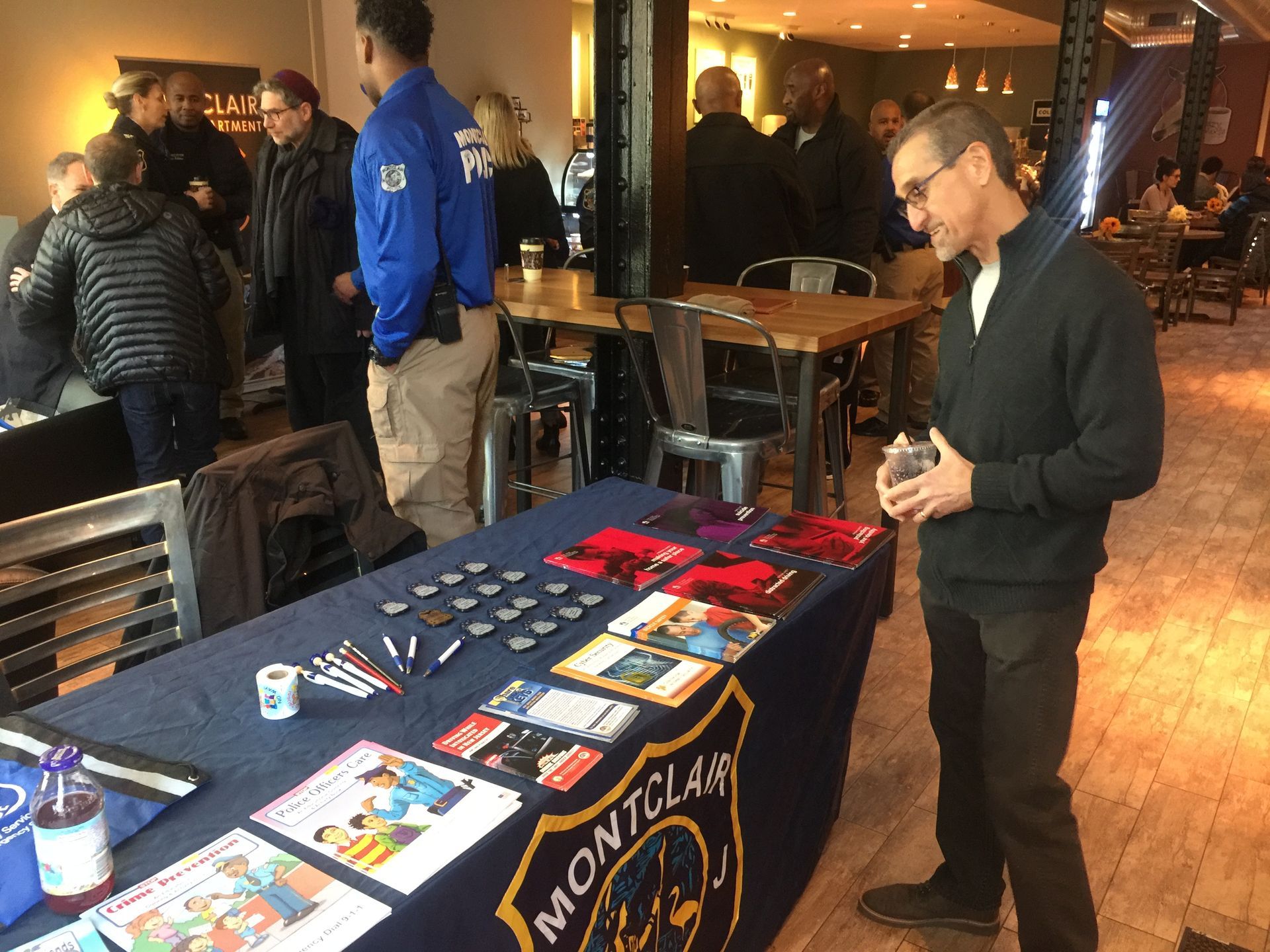 A man looking at a table with Montclair Police promotional items at an indoor event.