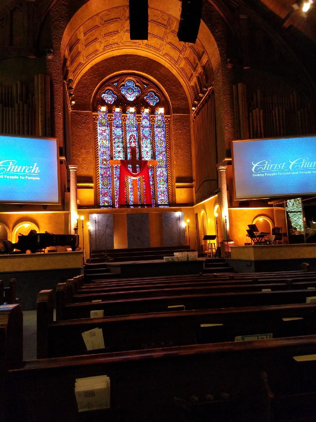 Interior of a church sanctuary, with pews, stained-glass window, and two screens with text.