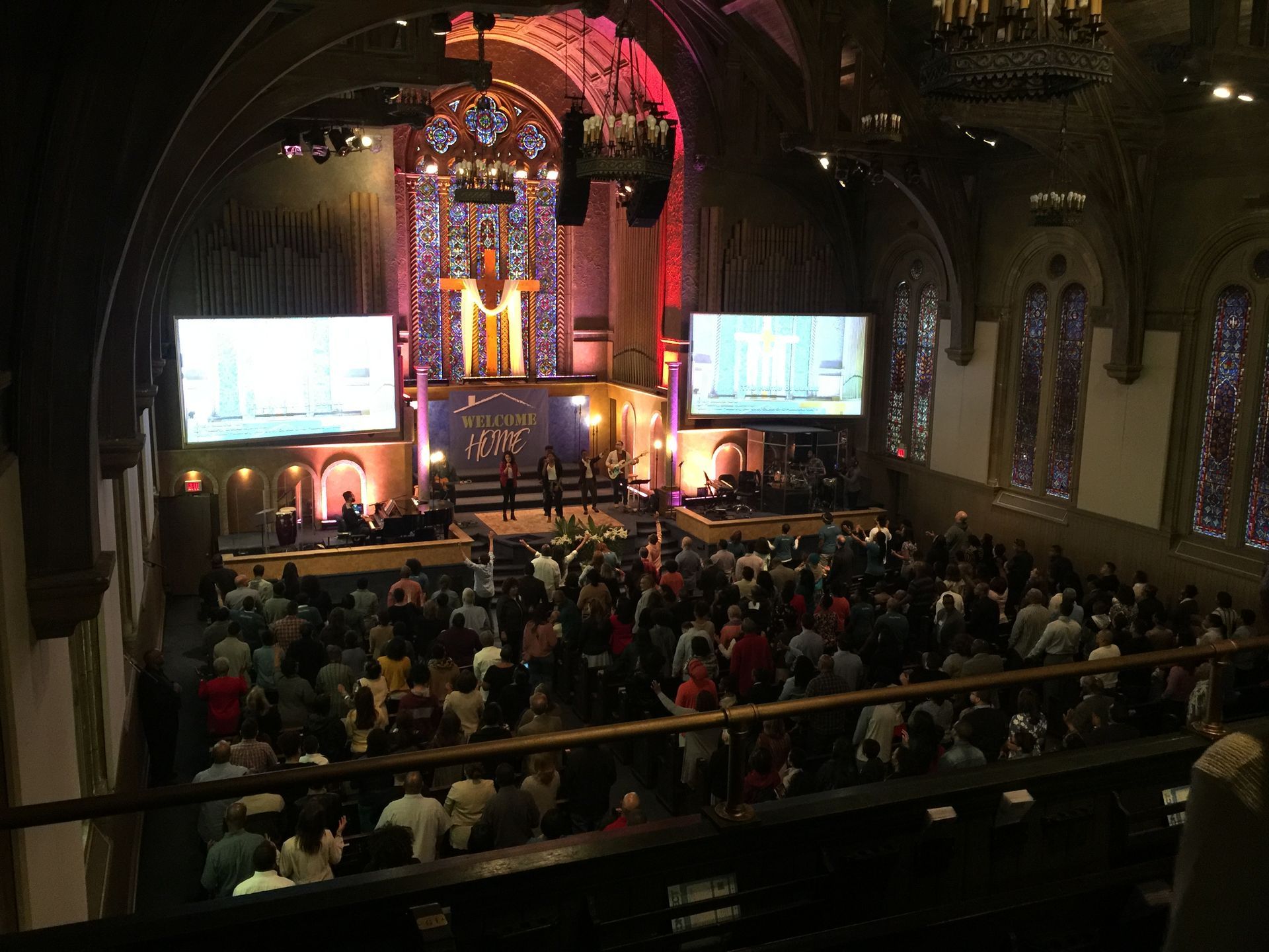 Audience in a church service, stage with screens, musicians, and stained glass.