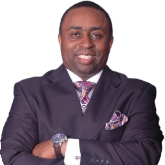Man in dark suit smiles, arms crossed, paisley tie and pocket square, watch visible.