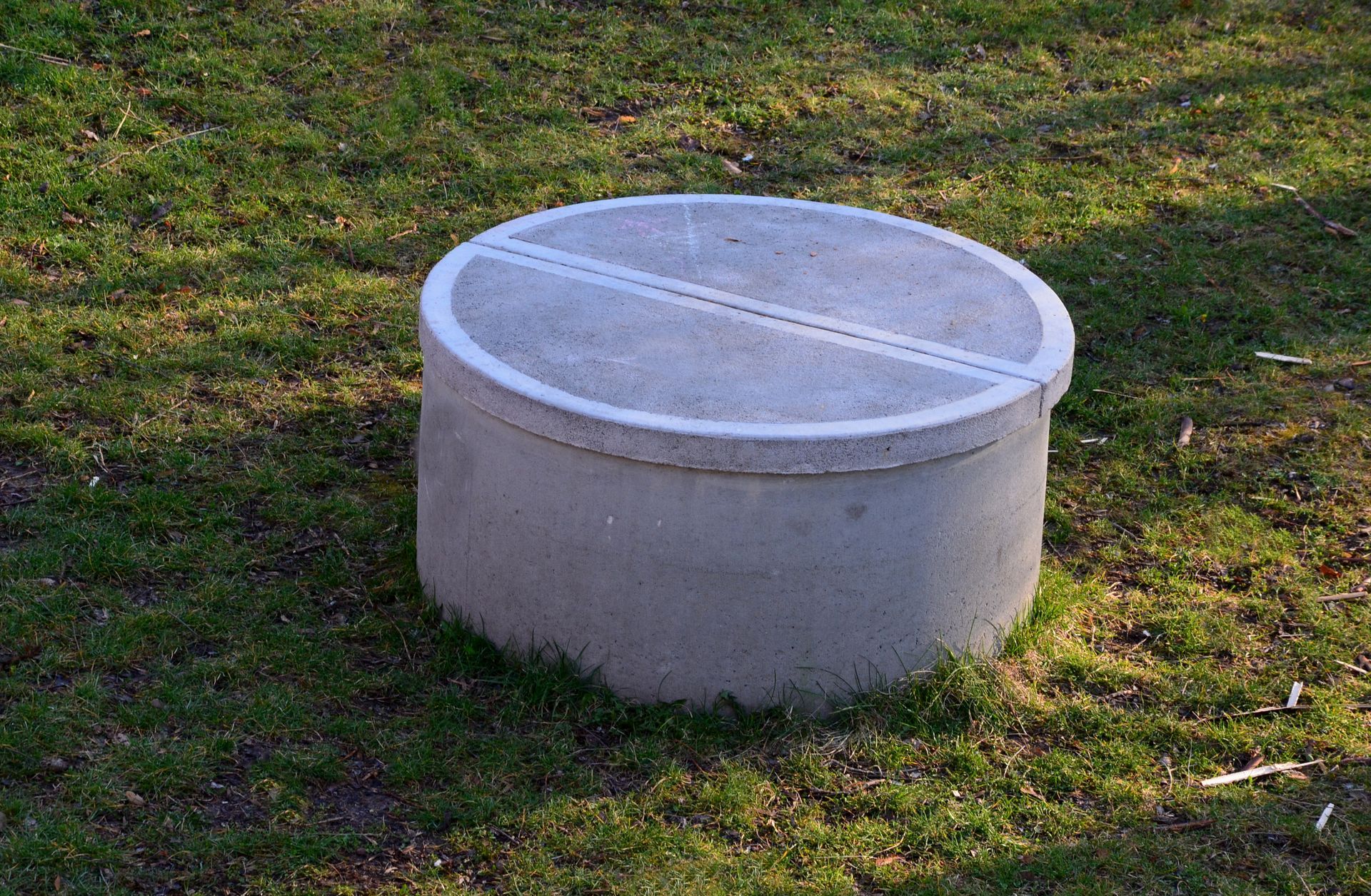 Round concrete utility lid on grass in a yard.