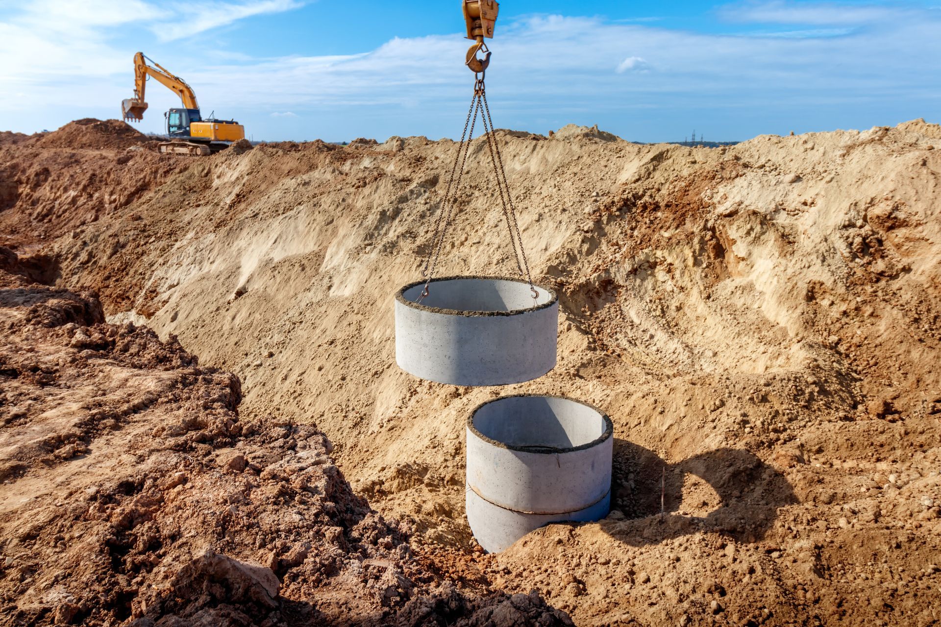 Excavator at a sandy construction site with two concrete pipe sections in a trench