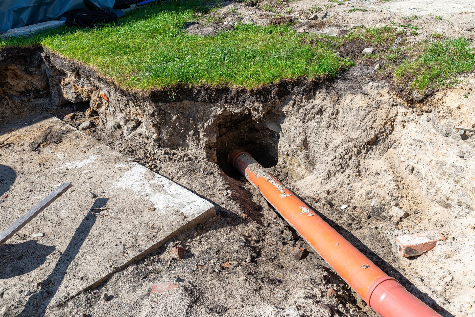 Orange pipe in a dug trench near a lawn, entering a hole under the ground