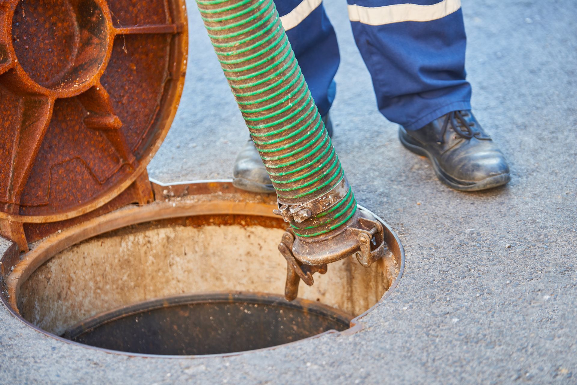 Worker opening a manhole with a green hose in a paved street