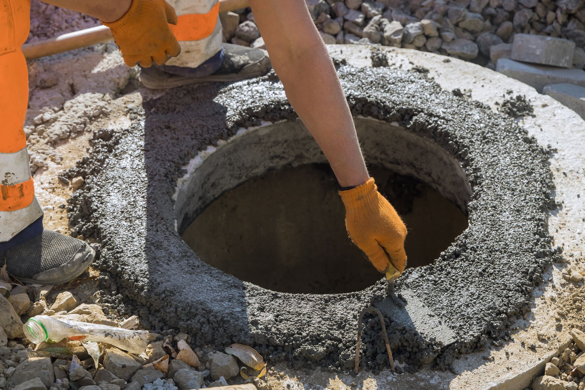 Worker placing concrete around a circular manhole opening at a construction site