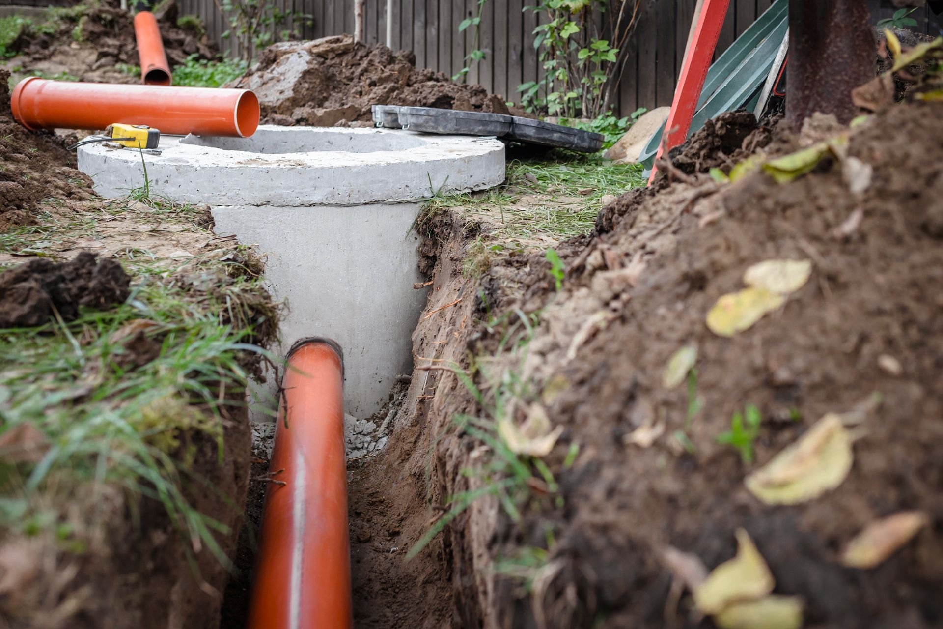 Orange pipes installed in a concrete utility chamber amid a muddy trench