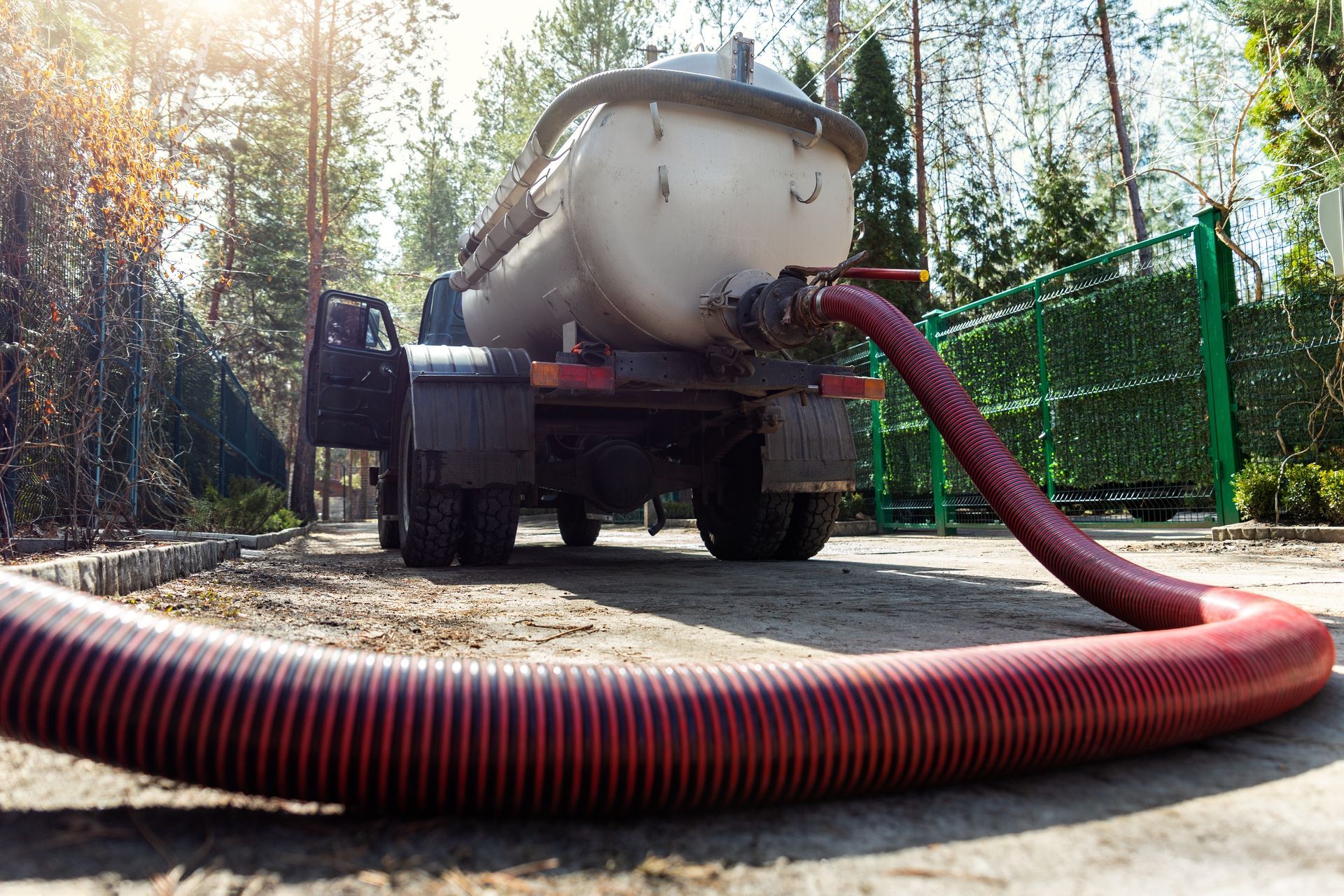 Vacuum truck pumping liquid through a red hose in a wooded outdoor area