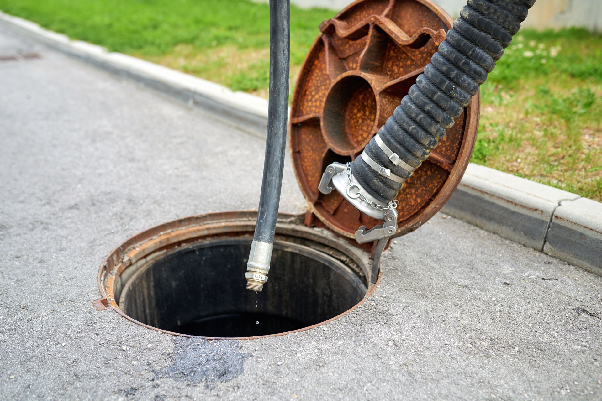 A vacuum hose cleaning a round manhole on a roadside sidewalk.
