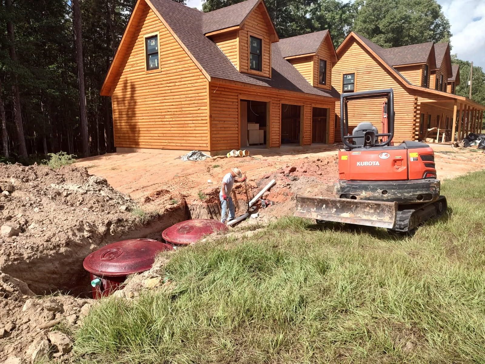 Orange excavator at a log house construction site with workers and dug-out trench