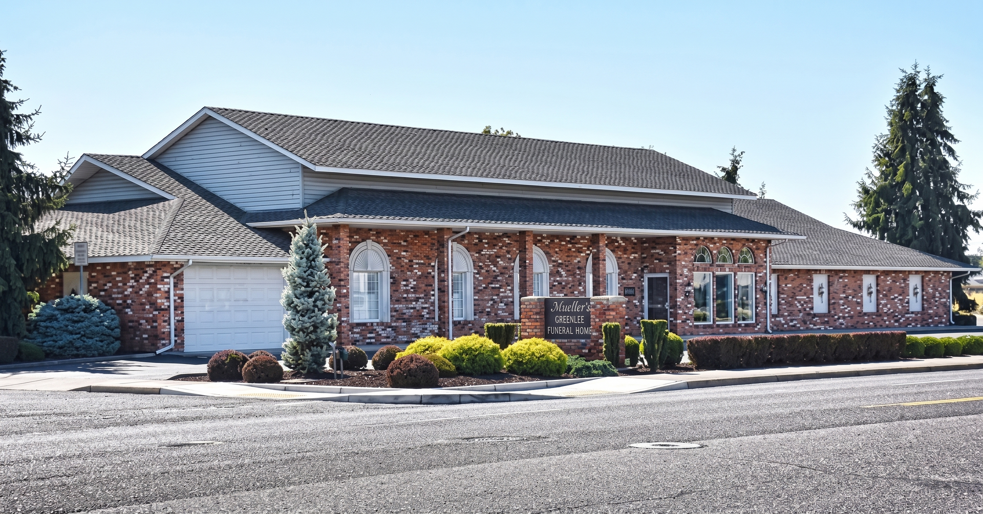 Single-story brick building with a gray roof and landscaped front, viewed from the street