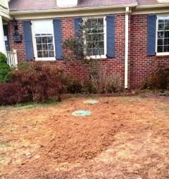 Bare dirt patch in front of a brick house with visible septic system access covers.
