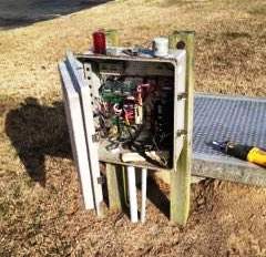 Open electrical box with wires, partially disassembled, next to a metal grate and a tool.