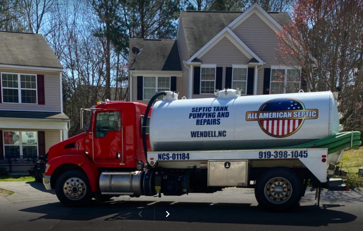 Red septic tank truck parked in front of houses; reads 