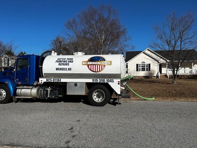 Blue septic tank truck pumping a house's septic system on a sunny day.