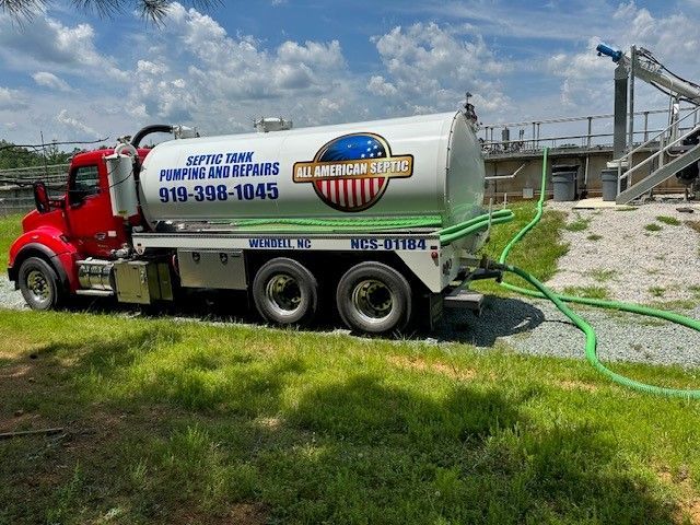 Red septic tank truck with white tank, parked on grass. Has company name and phone number.
