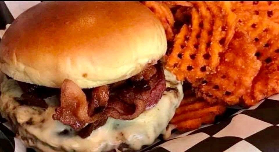 A close up of a hamburger and waffle fries on a checkered table cloth.