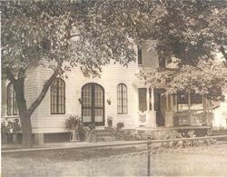 Sepia-toned house with arched windows, front porch, and large trees in front.