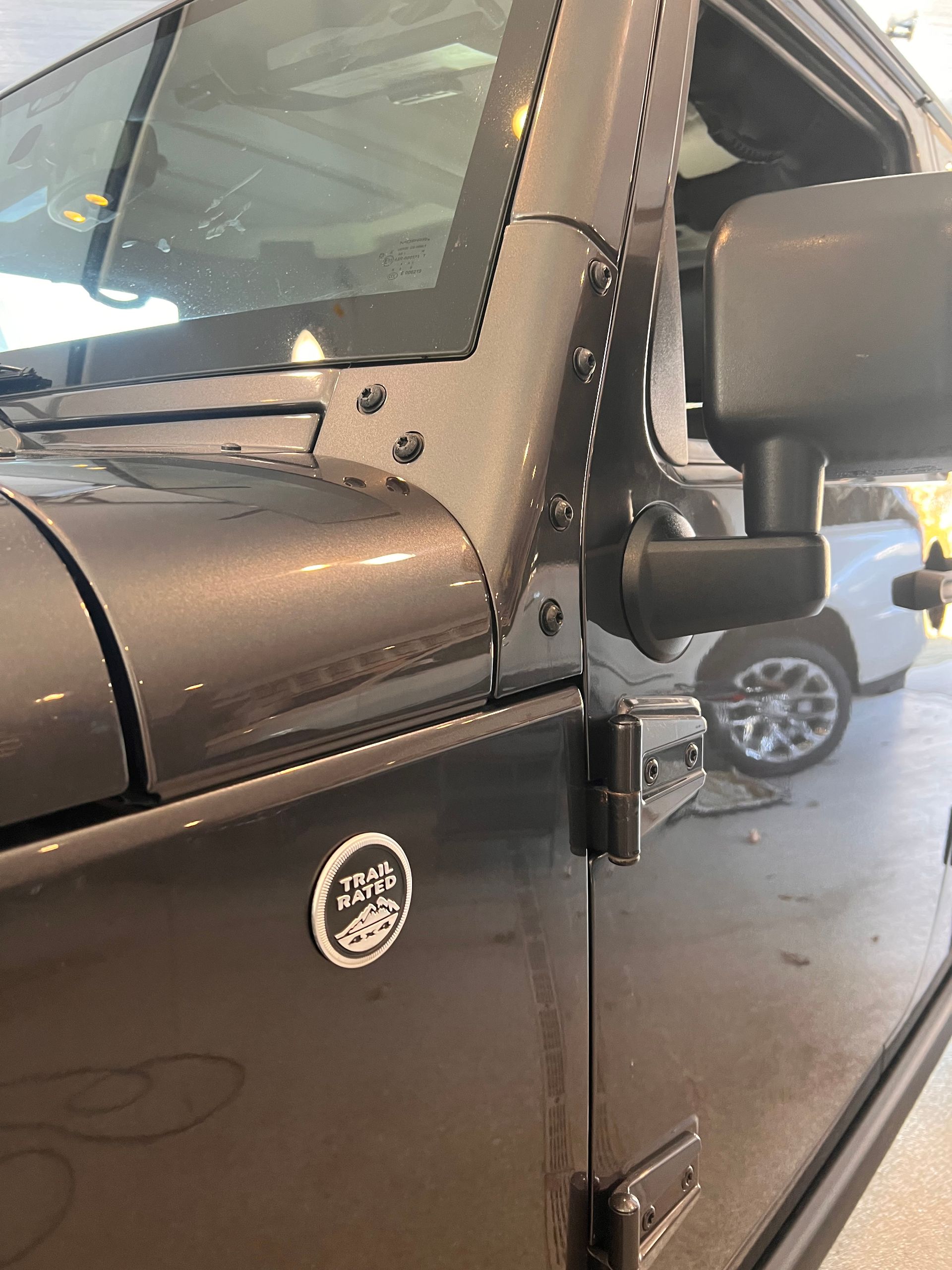 Close-up of the front driver-side pillar and door hinge of a dark gray Jeep with a small badge on the door panel.