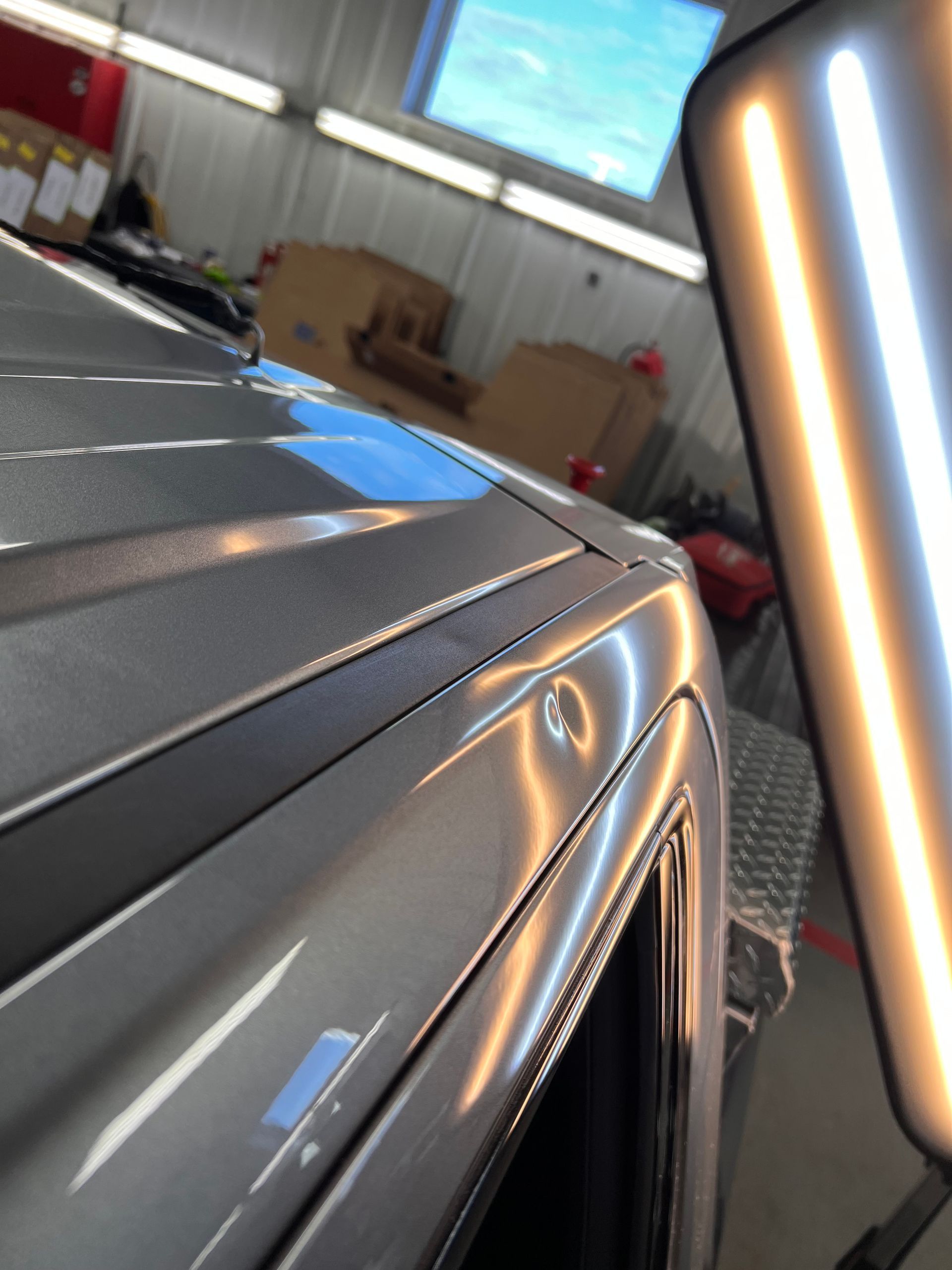 A dent on the roof edge of a silver car, highlighted by a PDR technician's specialized alignment light.