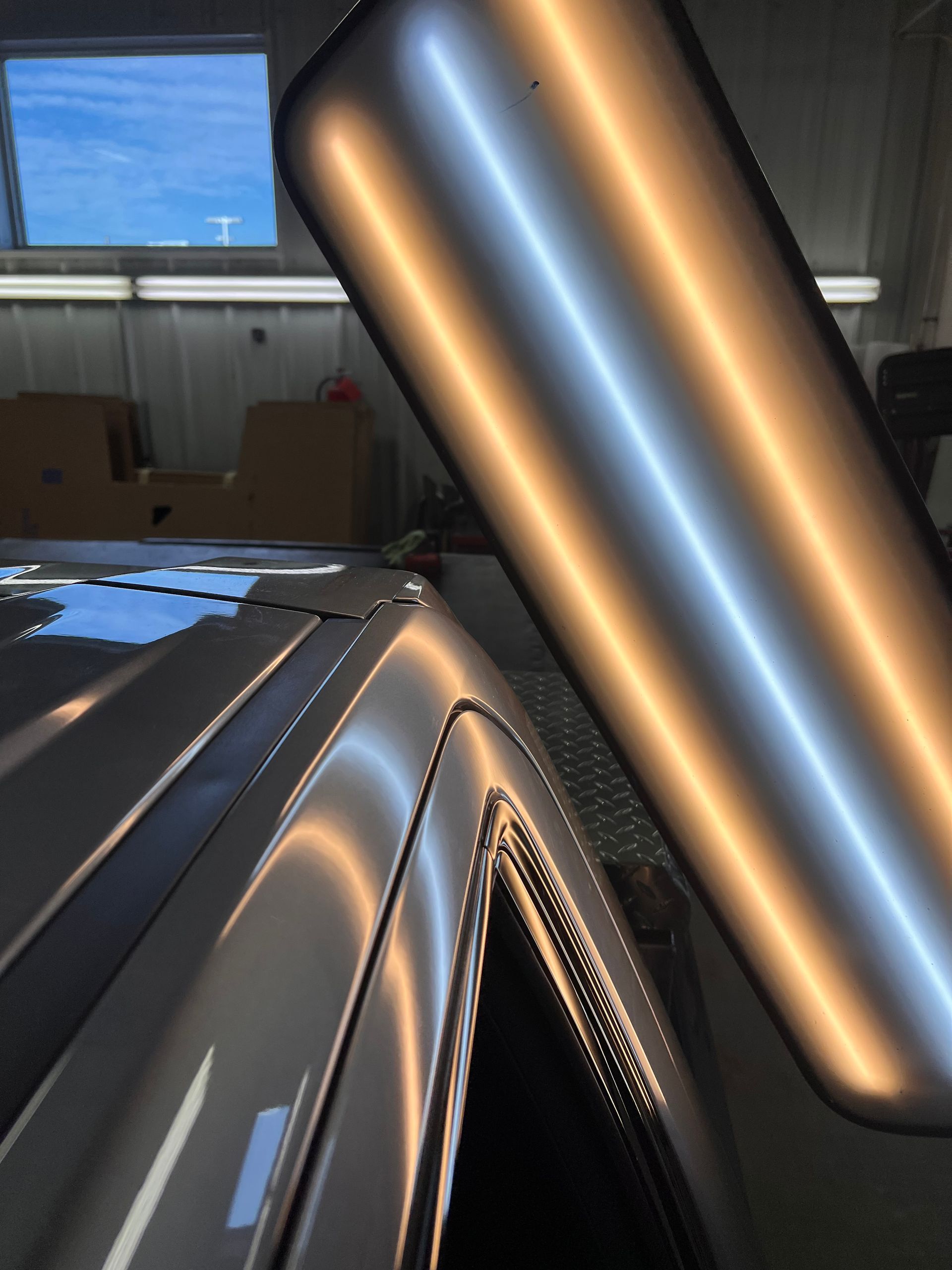 A PDR light board reflects on a car's roof and pillar, highlighting a dented surface for paintless dent repair.