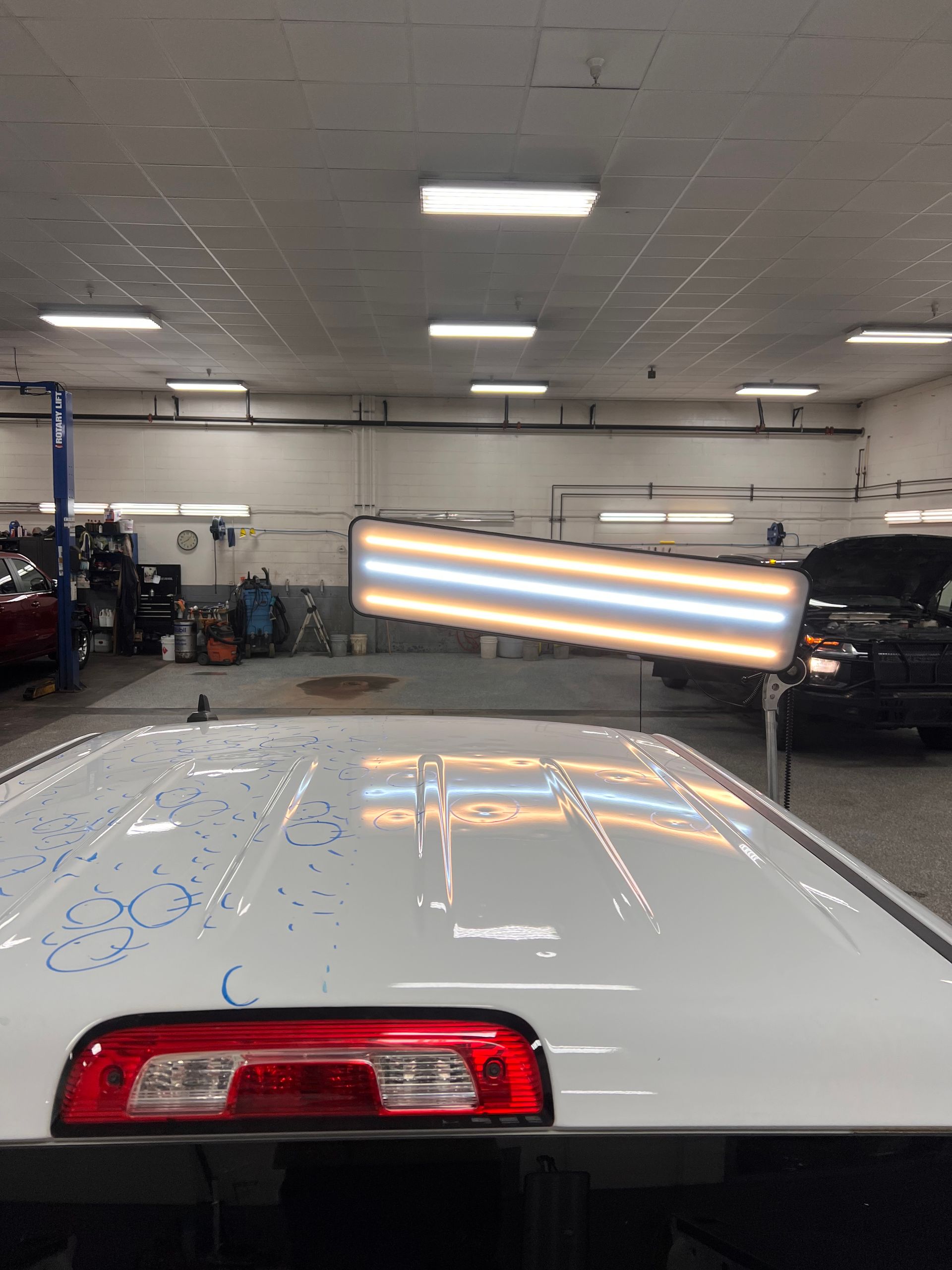 A white vehicle roof in a repair shop with blue markings and a professional lighting board used for dent inspection.