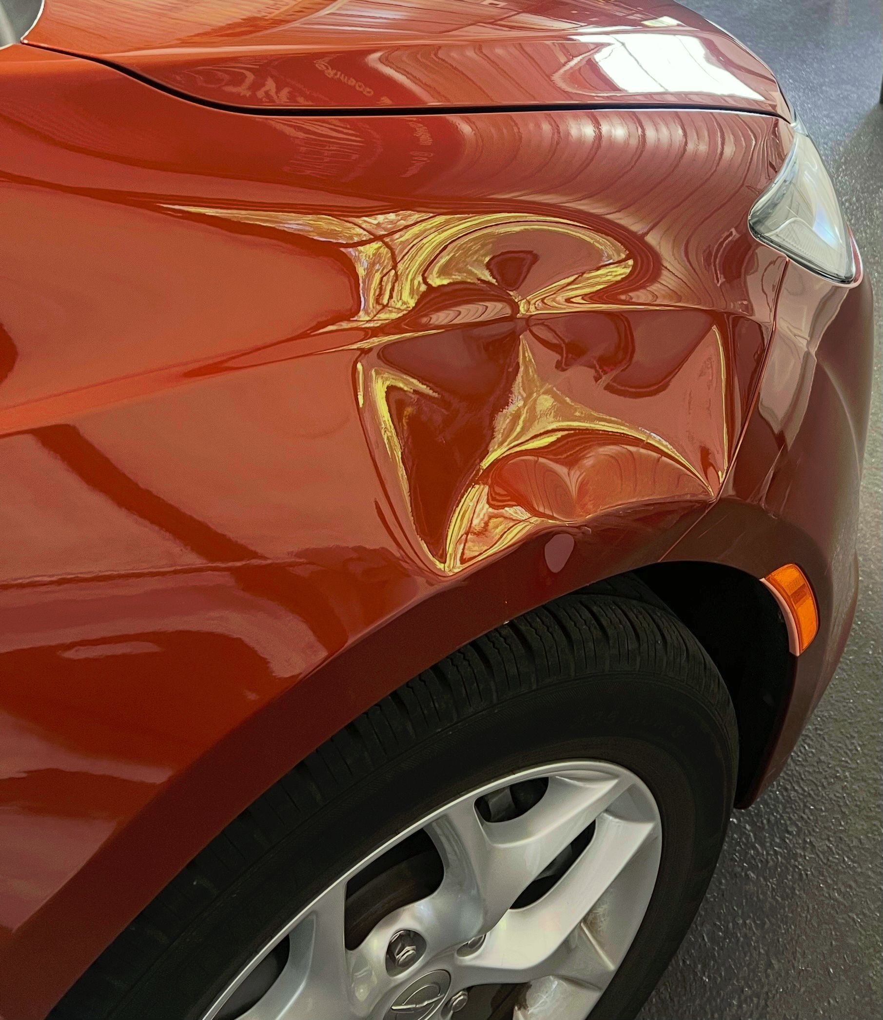 A large dent on the front passenger side fender of an orange car.