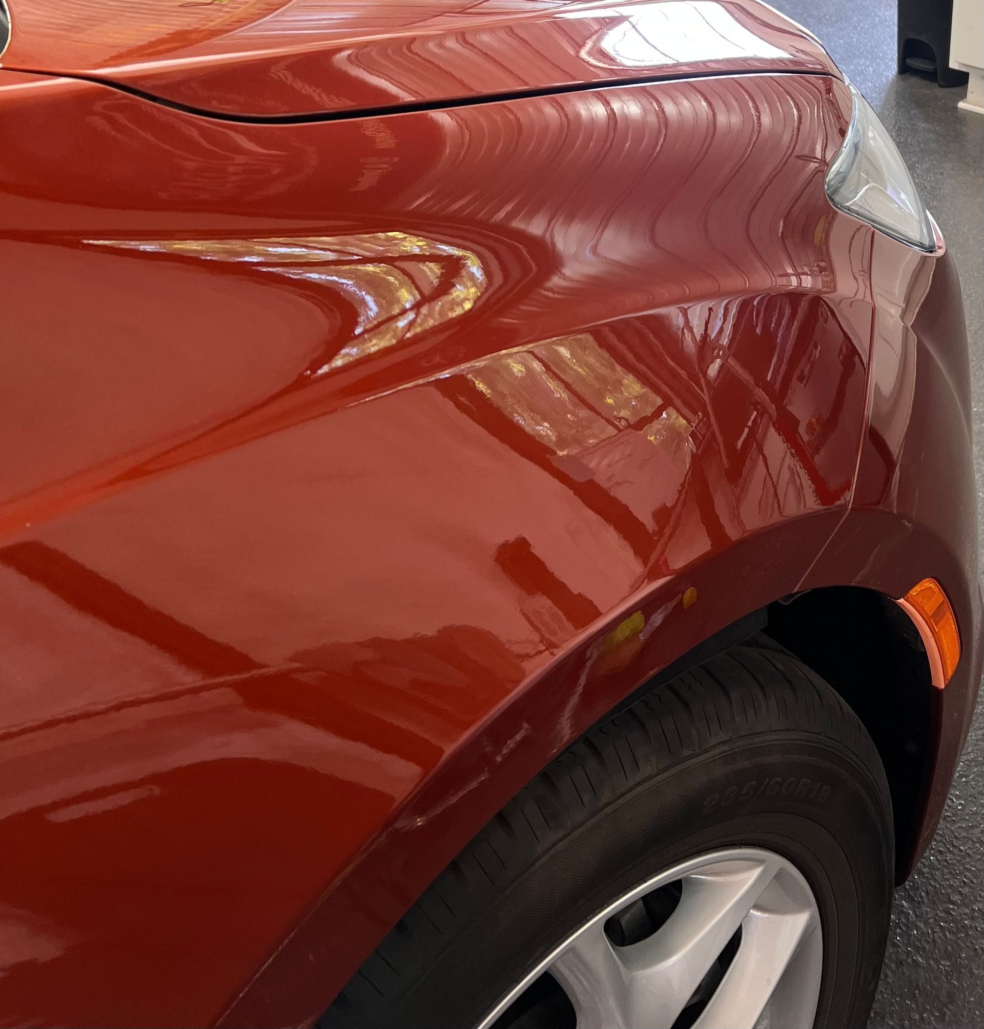 A close-up view of the front passenger-side fender and wheel of a metallic orange car parked on a grey floor.