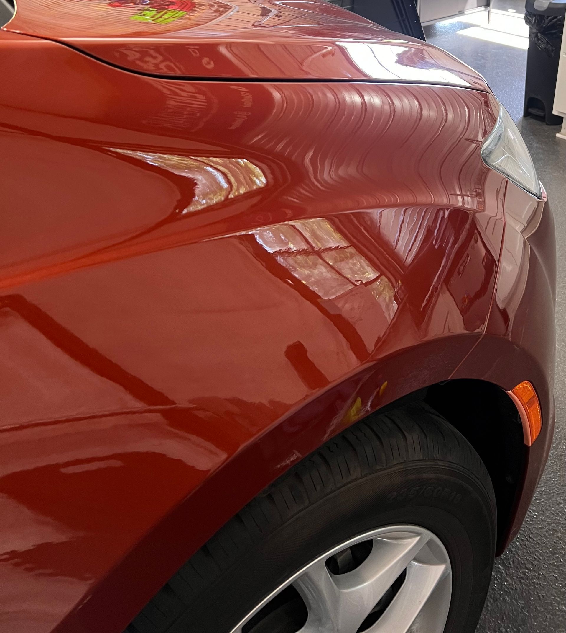 Close-up of a glossy, metallic red car fender and front tire parked on a gray surface.