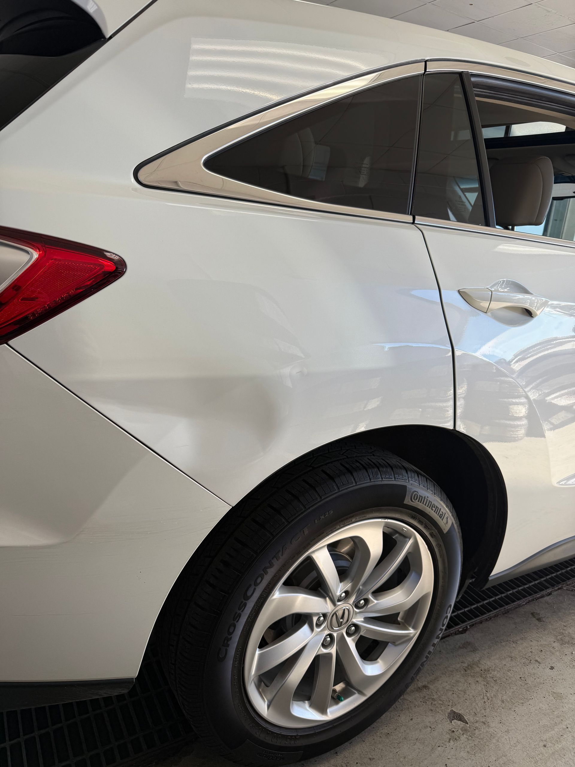 A white SUV showing a visible dent on the rear quarter panel above the rear wheel.