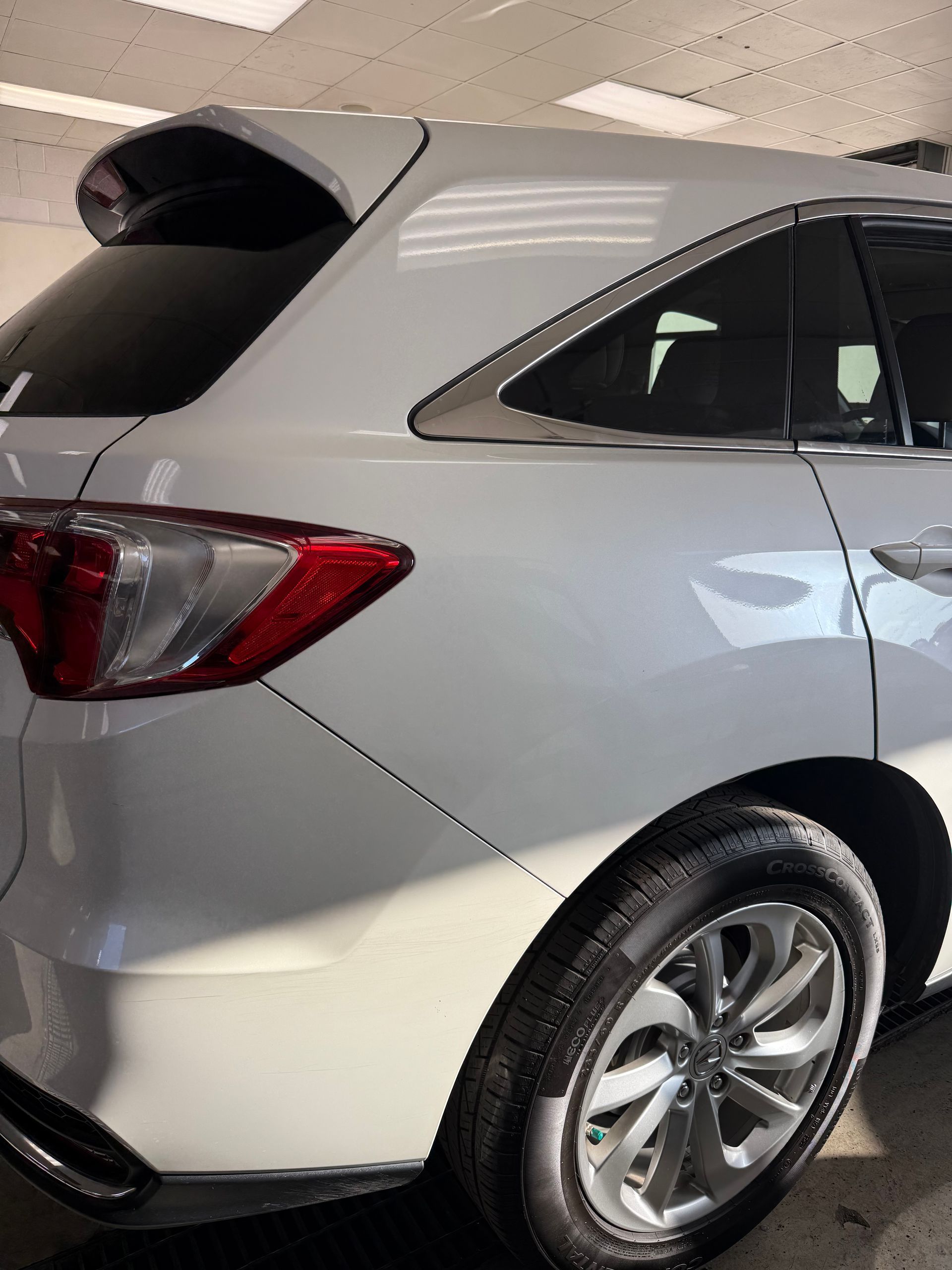A white SUV parked indoors, showing the rear passenger side, taillight, spoiler, and wheel.