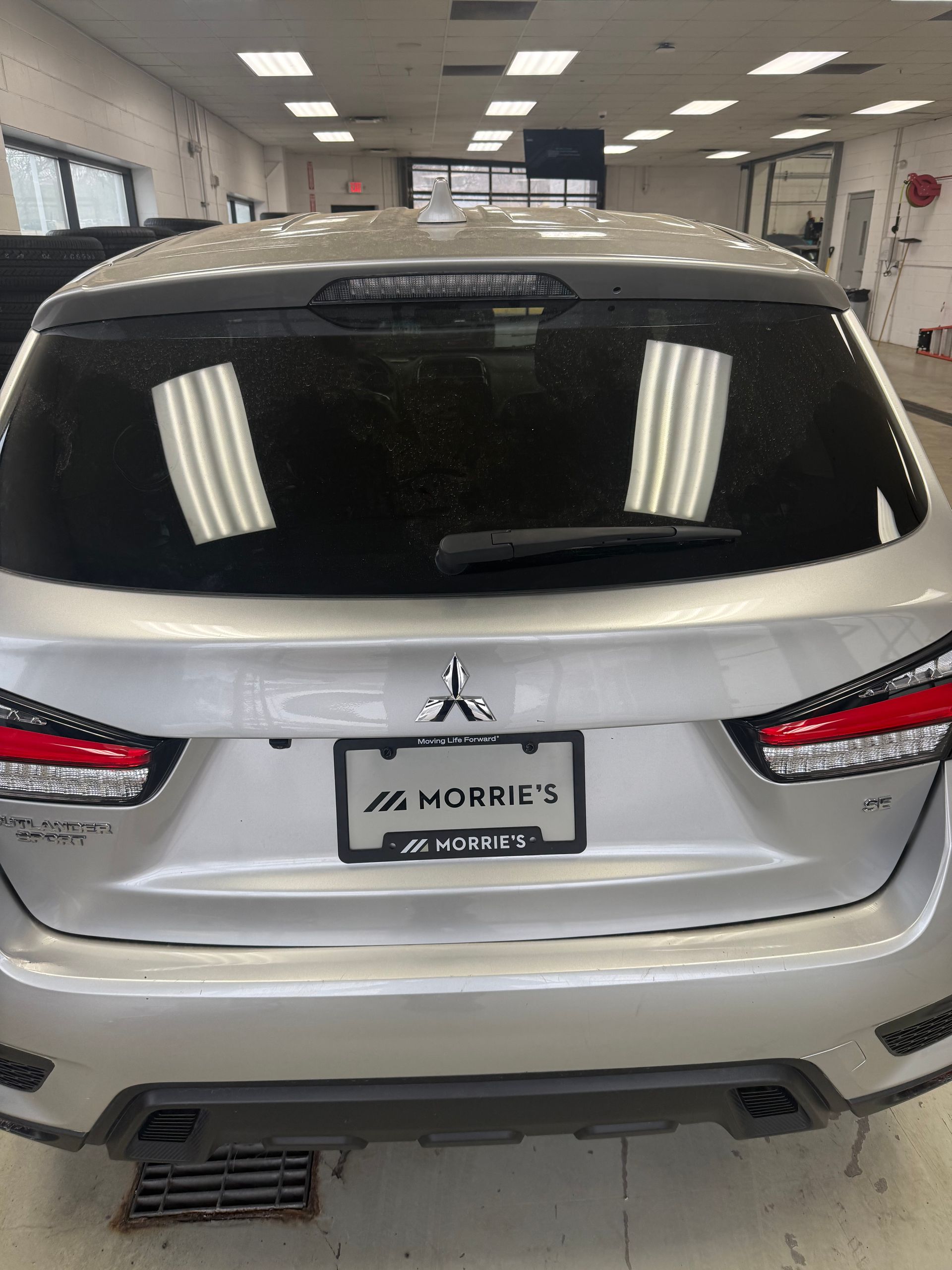 A silver Mitsubishi SUV parked inside a dealership, showing the rear view with a branded license plate cover.