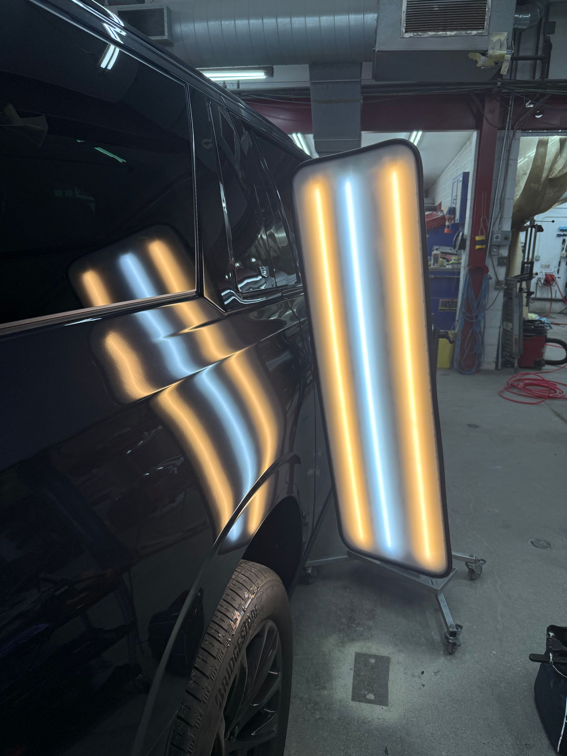 A shop light reflects off the dented side panel of a black car, highlighting the shape of the damage for repair.